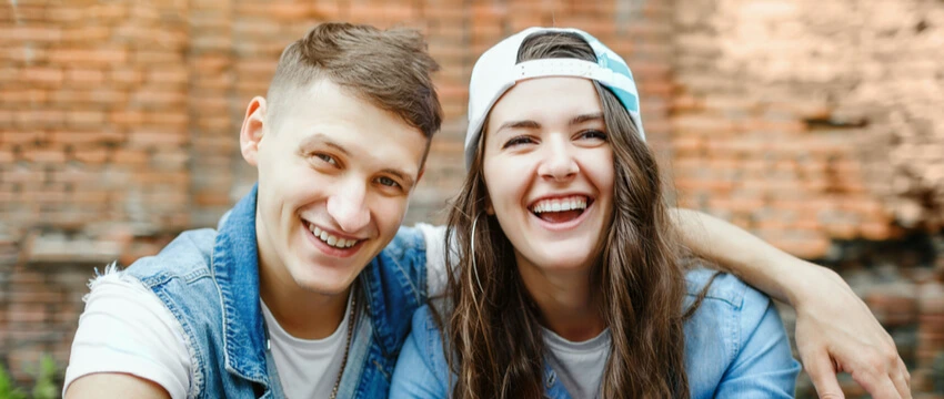 Young couple smiling together against a brick wall, highlighting preventative oral health care at Green Dental St Leonards.