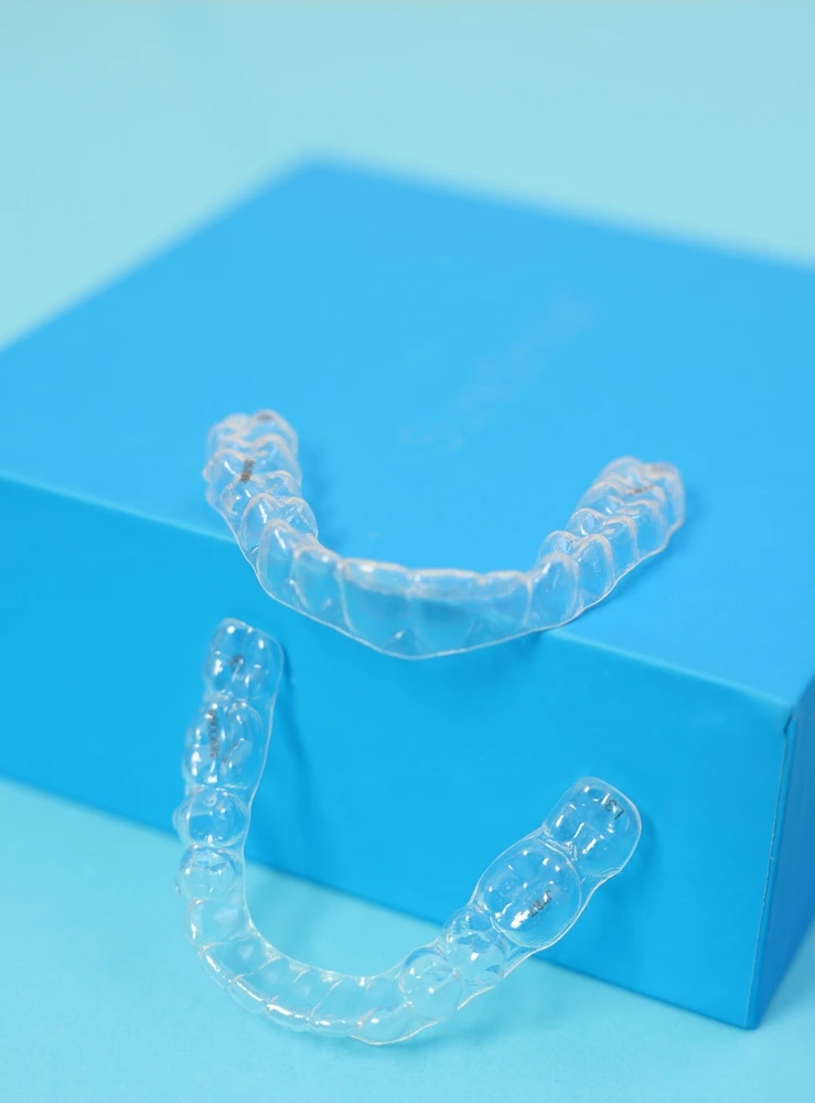 Pair of transparent clear aligners resting on a blue packaging box. Custom orthodontic care at St Leonards Green Dental.